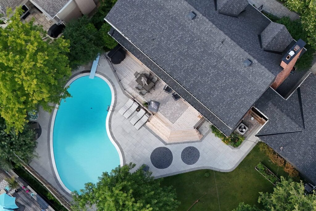 WLS Landscaping | Landscaping Around a Pool in Ottawa: What to Decide Before Anyone Digs Top-down aerial view of a freeform pool with a paver deck, cedar deck and curved patio built by WLS Landscaping